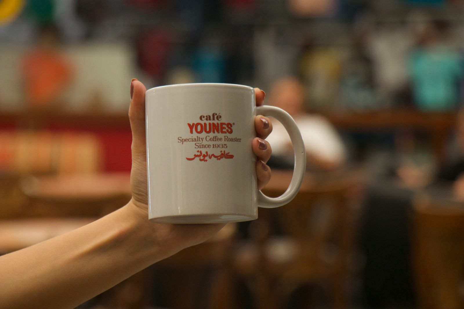 Café Younes branded mug held by a customer 