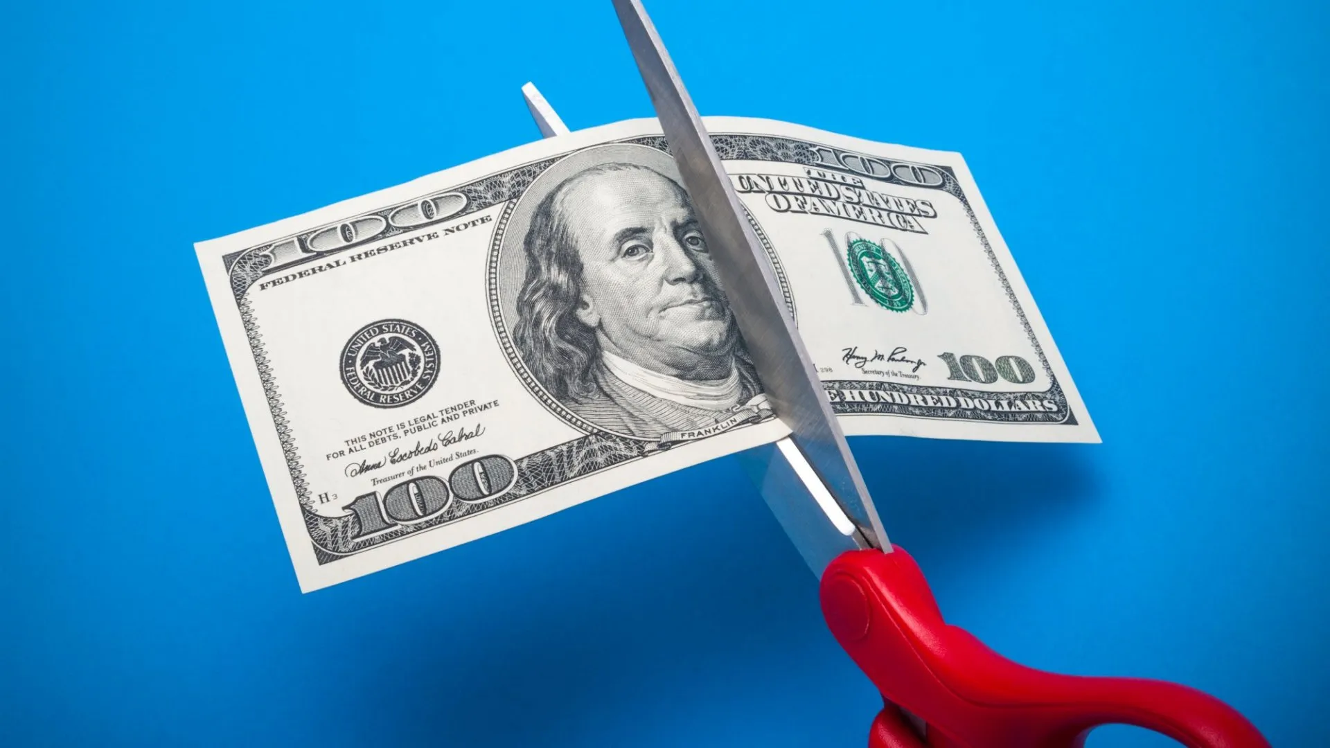 Someone is cutting the dollar bill in half to signify costs' reduction