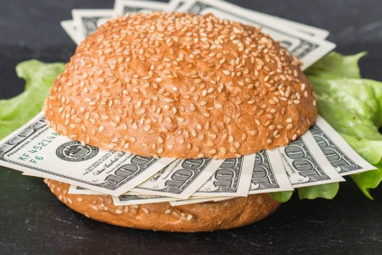 A picture of a burger with dollar bills inside of it indicating food inflation