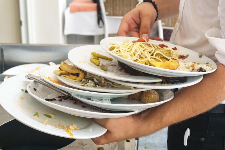 food wasted at restaurants: a waiter holding a pile of leftover plates