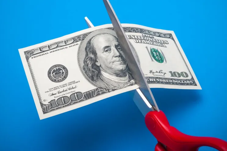 Someone is cutting the dollar bill in half to signify costs' reduction