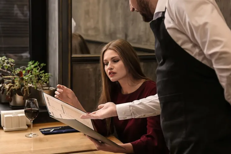 menu pricing strategies: a waiter helping a customer with the menu